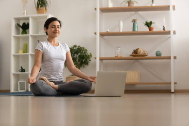 Serene millennial melez kadın dizüstü bilgisayardan önce meditasyon yapıyor.