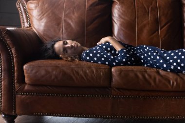 Yorgun genç bir kadın evdeki kanepede uyuyor.