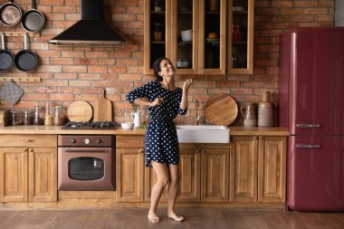 Mutlu genç kadın modern mutfakta dans ediyor.