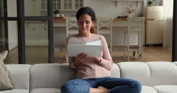 Relaxé millénaire jolie femme lecture livre, assis sur le canapé. — Video