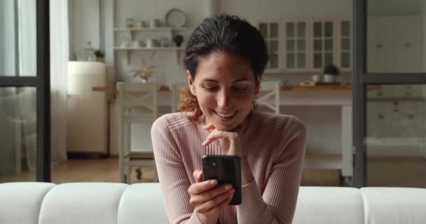 Glückliche junge Frau mit Smartphone, zu Hause auf Sofa sitzend. — Stockvideo