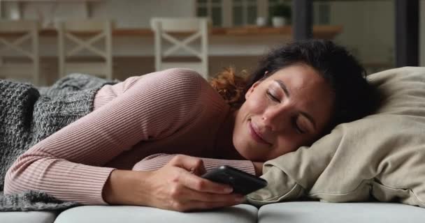 ソファに横たわっスマートフォンを使用してリラックスした100万人の女性. — ストック動画