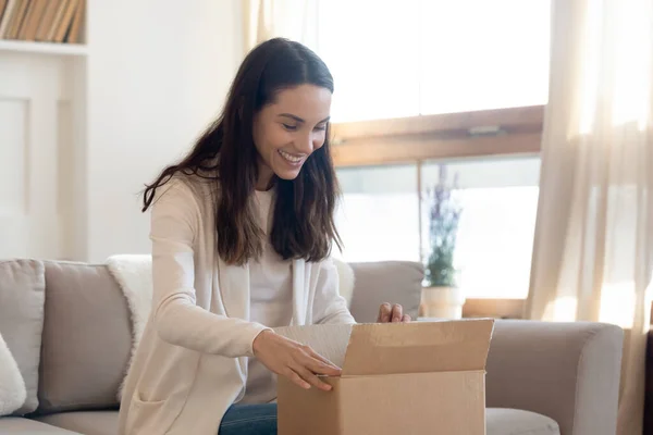 Dolblij nieuwsgierige vrouw openen kartonnen doos met pakket thuis — Stockfoto