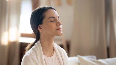 Kapalı gözlerle evde meditasyon yapan barışçıl bir kadın.