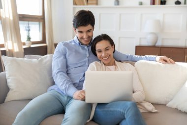 Mutlu genç çift dizüstü bilgisayar kullanıyor, birlikte kanepede dinleniyorlar.