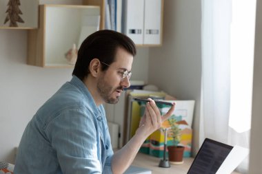 Konsantre genç işadamı telefon kaydedici kullanarak notları dikte ediyor.