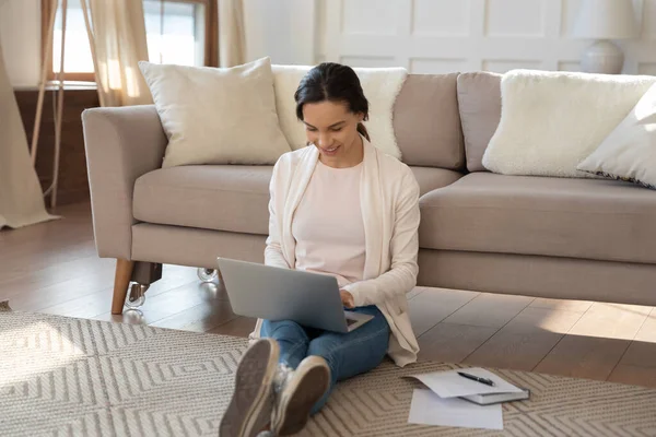 Usmívající se žena pomocí notebooku, sedí na teplé podlaze doma — Stock fotografie