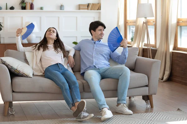 Vyčerpaný muž a žena mávají papírovými ventilátory, odpočívají na gauči — Stock fotografie