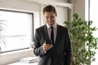 Gülümseyen kendine güvenen iş adamı telefon ekranına bakıyor.