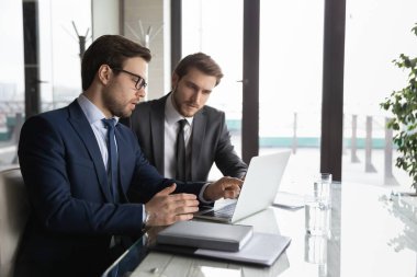 Kendine güvenen işadamı dizüstü bilgisayarı gösteriyor, yeni çalışanı eğitiyor.