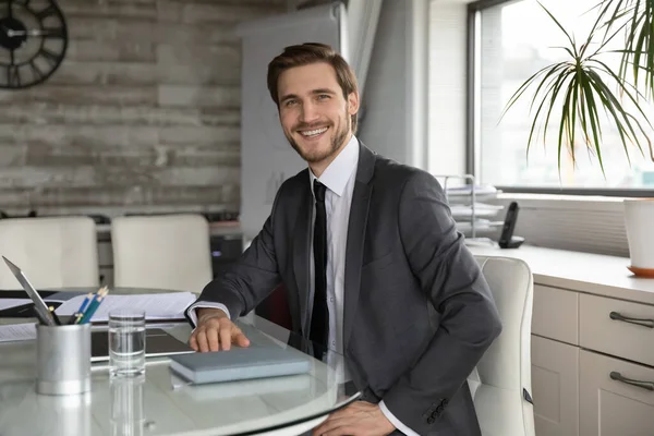 Портрет, улыбающийся уверенный бизнесмен, сидящий за столом в современном офисе — стоковое фото