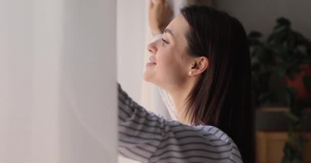Boldog fiatal nő néz ki az ablakon. — Stock videók