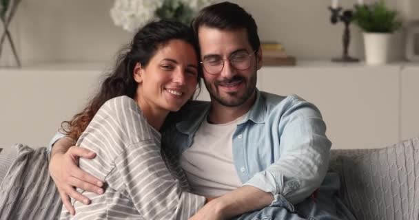 Ευτυχισμένο ζευγάρι αγκαλιάζει χαλαρώνοντας στον καναπέ χαμόγελο ματιά στην κάμερα — Αρχείο Βίντεο