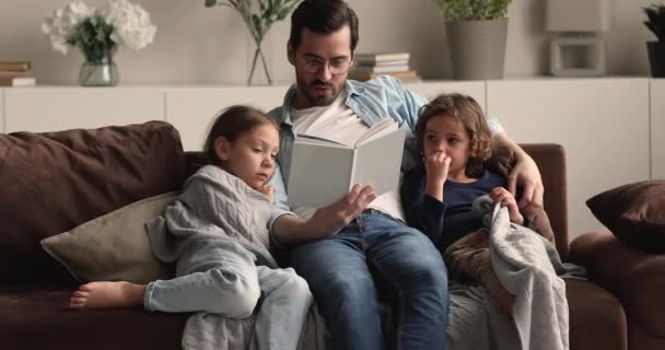 Kochający ojciec czytający książki synowi i córce — Wideo stockowe