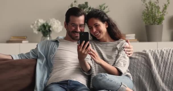 Birbirlerine aşık güzel bir çift. Kanepede akıllı telefonlarıyla sarılıyorlar. — Stok video