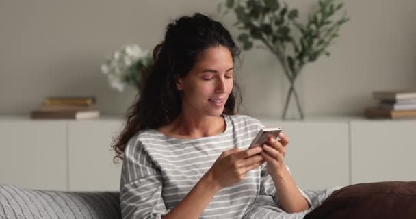 Entspannte Frau mit Smartphone sitzt auf Sofa im Wohnzimmer — Stockvideo