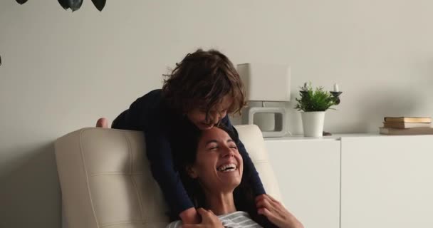 Γιος αγκαλιά γαργάλημα αγαπημένη μαμά κάθεται στην καρέκλα στο σπίτι — Αρχείο Βίντεο