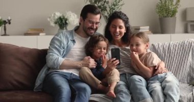 Çocuklu bir çift kanepeye uzanıp akıllı telefon kullanarak eğleniyor.