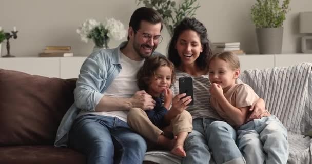 Paar mit Kindern entspannt auf Couch und hat Spaß mit Smartphone — Stockvideo