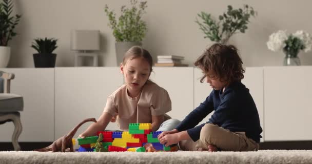 Niño y niña juegan constructor de plástico en la sala de estar — Vídeo de stock