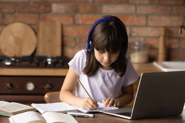 Close up little girl wearing headphones writing notes, studying online — Stock Photo, Image