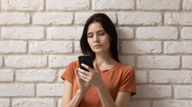 Kafasından vurulmuş ciddi bir genç kadın telefon kullanıyor, tuğla duvar altyapısı var.