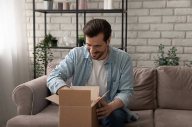 Meraklı genç adam paketleri boşaltıyor, koltukta oturuyor.