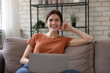 Dizüstü bilgisayarı olan mutlu bir kadının portresi rahat koltukta oturuyor.