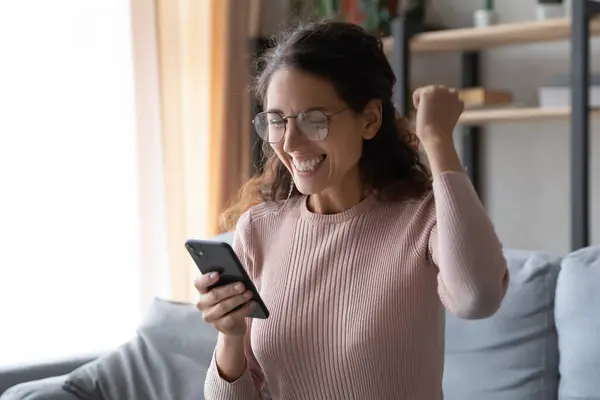 Overjoyed young woman in eyewear looking at mobile phone screen. — Stock Photo, Image