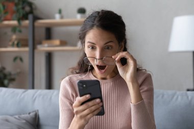 Akıllı telefon ekranına ağzı açık bakan duygusal genç bir kadın..