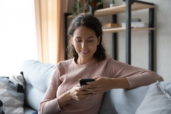 Relaxed young woman using smartphone sitting on sofa. — Stock Photo, Image
