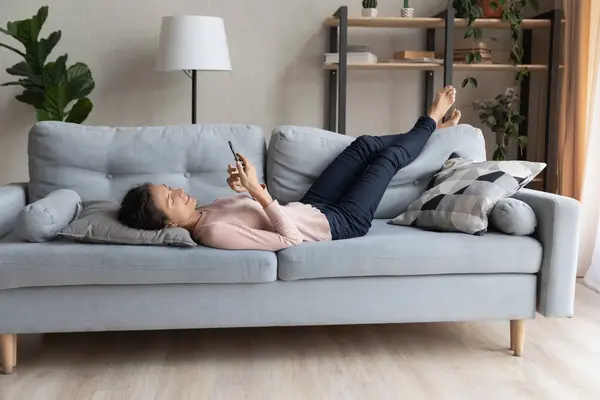 Femme millénaire détendue couchée sur le canapé, à l'aide d'un smartphone. — Photo