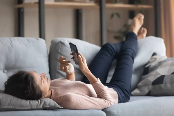 Joyeux jeune femme utilisant un téléphone portable, relaxant sur le canapé. — Photo