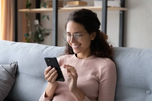 Happy millennial woman using mobile apps, sitting on sofa. — Stock Photo, Image