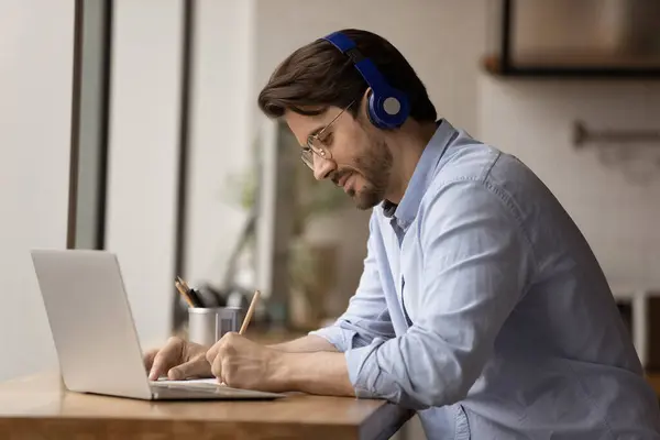 Diligent man student in earphones answering test questions on paper — Stock Photo, Image