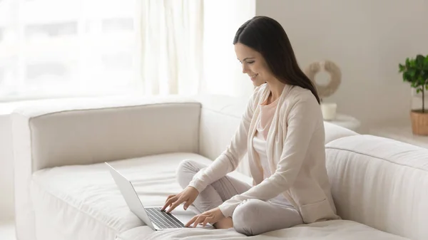 Gülümseyen genç kadın evde dizüstü bilgisayar kullanarak rahatlıyor. — Stok fotoğraf