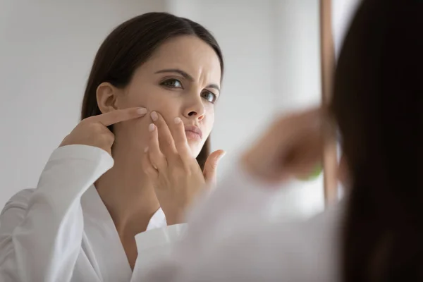 Unhappy woman look in mirror squeeze pimple — Stock Photo, Image