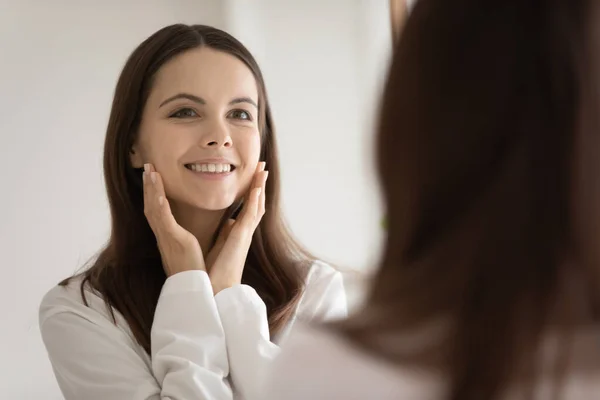Felice giovane donna guarda nello specchio toccare il viso sano — Foto Stock