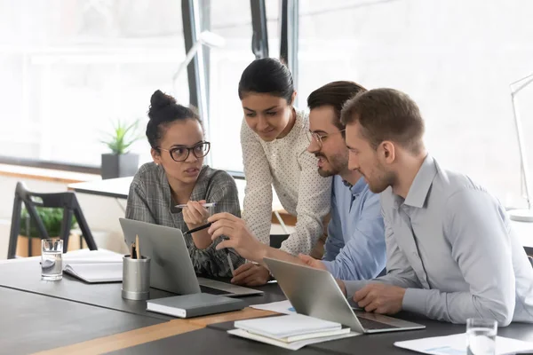 Mixed raced millennial employees talking at shared desk with laptops — Stock Photo, Image
