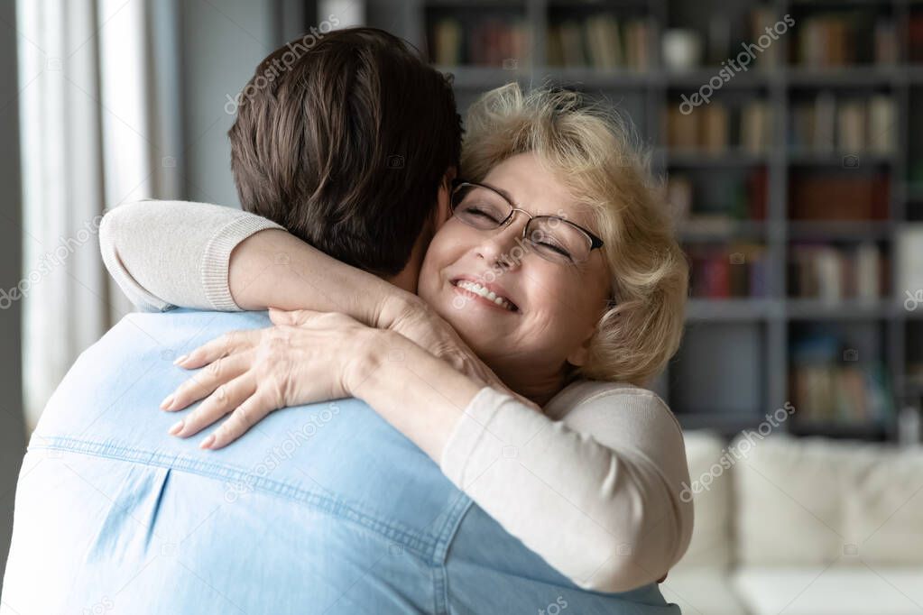 Sincere loving middle aged older woman cuddling affectionate grown son.