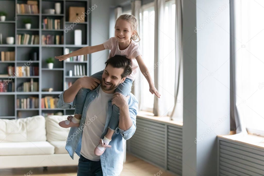 Happy young father carrying on shoulders laughing small daughter.