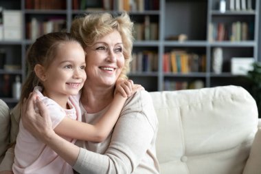 Smiling little girl cuddling loving caring older middle aged grandmother.