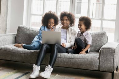 Dizüstü bilgisayar kullanan iki küçük çocuğu olan aşırı neşeli Afrikalı Amerikalı kadın.