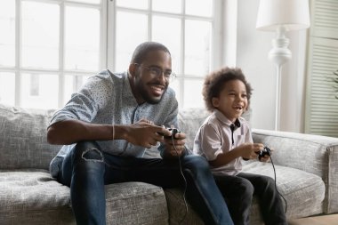 Coşkulu Afrikalı Amerikalı baba ve oğlu video oyunu oynuyorlar.