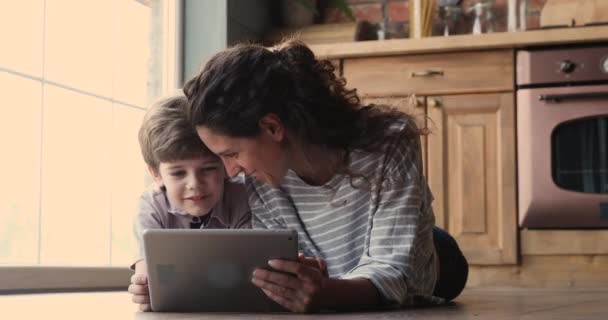 Glückliche Zweierfamilie mit digitalem Tablet auf dem Boden in der Küche liegend. — Stockvideo