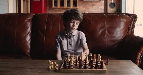 Сосредоточенный маленький милый мальчик играет в шахматы один дома. — стоковое видео