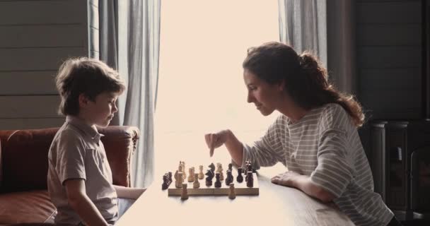 Liten pojke njuter av att lära sig spela schack med mamma. — Stockvideo