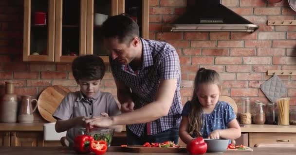 Caring young father teaching small adorable kids cooking. — Video