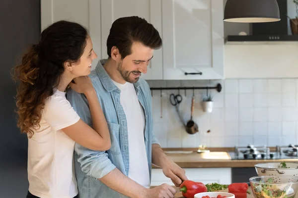 Minnettar eş, salata hazırlamakla meşgul kocanın omzunu kucaklıyor. — Stok fotoğraf