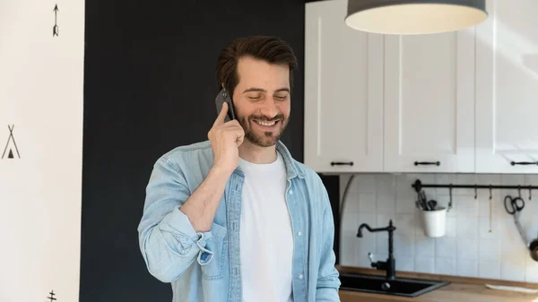 Felice maschio millenario coinvolto in una piacevole conversazione telefonica in cucina — Foto Stock